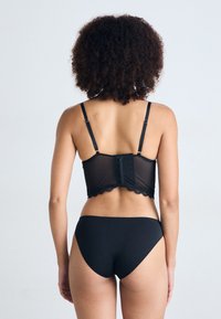 Zwart lingerieset met een sheer panel en een kanten rand, voorzien van verstelbare bandjes. De achterkant heeft een haak-en-oogsluiting met subtiele details.