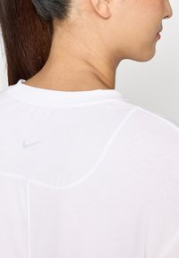 Bjela Nike majica s okruglim izrezom, prozračna tkanina i mali sivi logo blizu stražnjeg izreza, s glatkom teksturom.