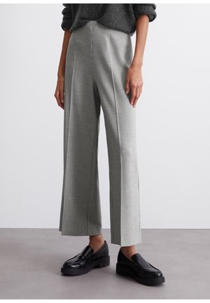 Vrouw die grijze wijde geruite broek, zwarte plateau loafers en een donkergrijze trui met opgerolde mouwen draagt.