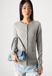Szary wełniany kardigan z okrągłym dekoltem, guzikami z przodu i kieszeniami. Towarzyszy mu mała niebieska torba z dżinsu. Styl casualowy z luźnym krojem.