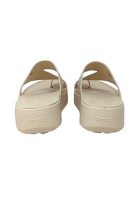 Sandali platform beige con ampia fascia, texture liscia e suola leggermente elevata. Logo "Crocs" visibile nella zona del tallone.