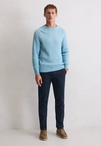 Hellblauer, gerippter Pullover mit Rundhalsausschnitt, kombiniert mit dunkelblauen Hosen und braunen Wildlederschuhen. Glatte Textur und figurbetontes Design.