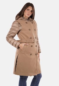 Trench coat beige con maniche a cappuccio rigonfie color sabbia, design doppiopetto, tasche laterali e una cintura abbinata in vita.