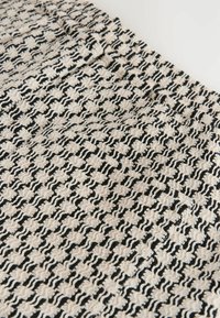 Tissu texturé noir et blanc avec un motif de carrés ondulés en relief et un détail de poche latérale avec couture cachée.