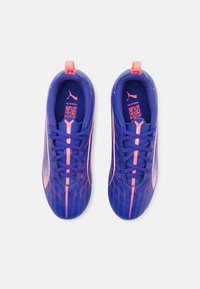 Scarpe sportive con tomaia in rete viola con accenti rosa, dettagli testurizzati, lacci piatti e un'impugnatura sul tallone.