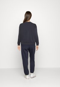 Felpa in navy con strisce e pantaloni coordinati, dotati di polsini a coste, con una vestibilità comoda. Texture liscia e design semplice.