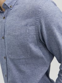 Camisa de botones azul con estampado, con un bolsillo en el pecho y cuello redondeado. Hecha de una tela texturizada con un sutil aspecto jaspeado.
