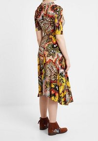 Blommönstrad klänning med korta ärmar, figurnära midja och utsvängd kjol i livfulla färger. I kombination med bruna fransade ankelskor.