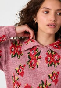 Roze trui met bloemenpatroon in rood en groen, kraagontwerp, gebreide textuur, geribde manchetten en een relaxte pasvorm.