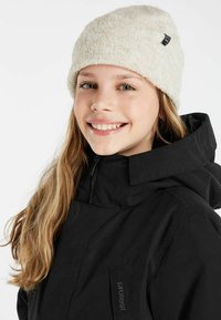 Zwarte waterdichte jas met een hoge kraag en ritssluiting. Beigebruine gebreide muts met een gestructureerd patroon en een klein zwart label.