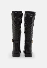 Stivali alti neri in faux leather con zip laterali, cinghie regolabili e fibbie in tono oro, dotati di una suola piatta in gomma e una finitura texturizzata.