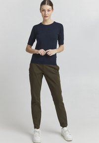 Navy short-sleeve knit top paired with olive green tapered pants, featuring a smooth texture and casual white sneakers.