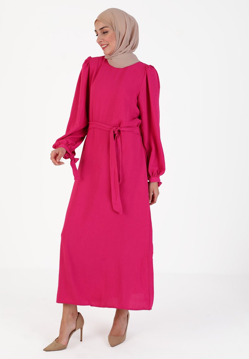Long pink dress made of lightweight fabric with puffed sleeves and a tie belt at the waist, paired with beige high-heeled shoes.