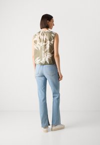 Ärmlös blus i olivgrön med vitt blommönster, med samlad halsringning, kombinerad med ljusblåjeans och vita sneakers.