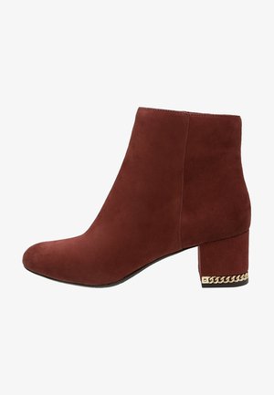 Bota de ante marrón hasta el tobillo con tacón de bloque, que presenta un detalle de cadena dorada a lo largo de la base del tacón.