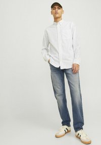Camisa de botones a rayas blancas y azules con un bolsillo en el pecho, combinada con jeans azul claro y zapatillas blancas con acentos verdes.