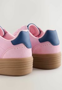 Baskets en daim rose avec un accent en cuir bleu marine au talon et une semelle en caoutchouc brun texturé. Elles présentent une forme arrondie et un col rembourré.