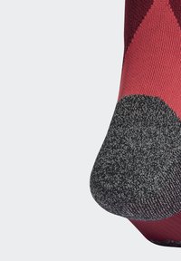 Ponožka s červeným a čiernym vzorom, ktorá má textúrovanú šedú špičku, rebrovaný dizajn blízko vrchu a hladký povrch po celom obvode.