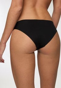 Slip bikini nero con una texture liscia, design a vita bassa e copertura minima, caratterizzato da linee pulite e senza elementi hardware visibili.