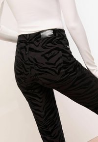 Mustad teksad, millel on tekstuuriga, sametilaadne materjal ja must-hall zebra triipmuster. Sisaldab tagaosalisi taskuid ja õmblusdetailide.