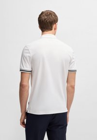 Biała koszulka polo z kontrastującymi czarno-białymi paskami na rękawach. Krótkie rękawy i klasyczny kołnierzyk. Gładka tekstura, luźny krój.