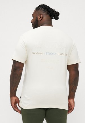 Cremefarbenes T-Shirt mit kurzen Ärmeln, das auf der Rückseite mit erhabenem Text versehen ist. Hergestellt aus weichem Material, entworfen für eine lockere Passform.