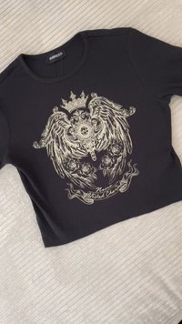 Black cropped t-shirt featuring a detailed silver graphic with wings, crown, and roses. Ribbed texture, round neckline, and short sleeves.