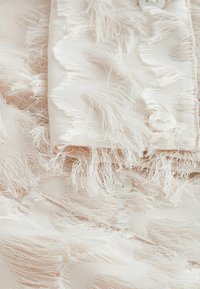 Gros plan sur un tissu blanc avec une texture effilochée en zigzag et de petits boutons blancs sur un poignet plié.