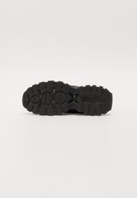 Semelle de chaussure de sport noire avec un motif de grip épais et texturé et un design de semelle distinct; le matériau en caoutchouc offre durabilité et traction.