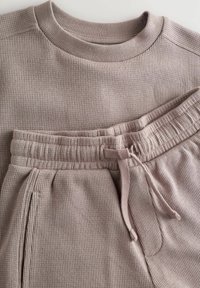 Svetlohnedý rebrovaný sveter a zodpovedajúce tepláky, ktoré majú okrúhly výstrih, elastický pás a detaily so šnúrkou.