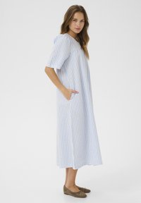 Modra in bela črtasta dolga obleka s kratkimi rokavi, ki ima stranske žepe in sproščen kroj. Izdelana iz lahkega materiala z mehkobo na dotik.