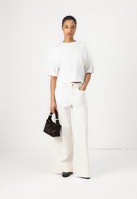 Witte cropped t-shirt met korte mouwen, gecombineerd met wijde witte broek. Houdt een kleine zwarte fluwelen handtas vast. Gladde stof, minimalistisch ontwerp.