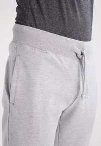 Gray sweatpants with a soft texture and elastic waistband, featuring a drawstring and side pockets, shown from a side angle.