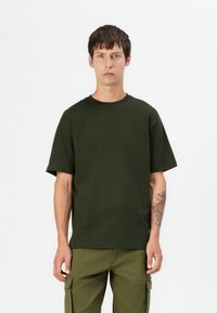 Dark green short-sleeve t-shirt made of cotton, featuring a crew neckline and a relaxed fit. Worn with matching cargo pants.