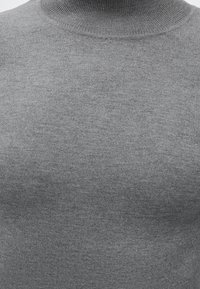 Tissu tricoté gris d'un pull à col montant présenté en gros plan, mettant en valeur la texture et les détails des coutures.