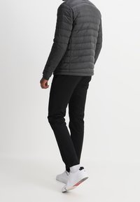 Harmaa puffatakkia, jossa on vaakasuora tikkaus, mustat housut ja valkoiset lenkkarit. Takissa on sileä pinta ja istuva muotoilu.