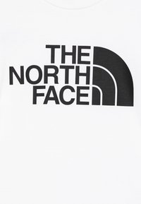 Fehér póló, melyen egy nagy fekete logó szöveg található: "THE NORTH FACE", jellegzetes ívelt formával a dizájnban. Pamut anyagból készült, sima tapintású.