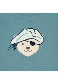 Lichtblauwe trui met een geborduurd berenhoofd in piratenthema, met een witte hoed, een zwarte ooglap en beige gezichtsdetails.