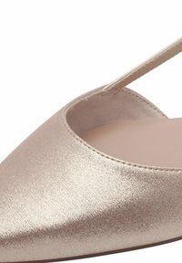 Boty s špičatou špičkou vyrobené z metalického růžového zlata, s hladkým povrchem a jedním páskem. Otevřený výřezový design odhalený po stranách.