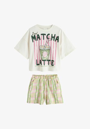 Biały top z krótkim rękawem z napisem „Iced Matcha Latte” i grafiką napoju, zestawiony z różowo-zielonymi szortami w paski z elastyczną talią.