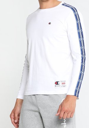 Langarm-Hemd aus weißer Baumwolle mit seitlichen blauen Musterstreifen und einem kleinen Logo auf der Brust. Hat einen runden Ausschnitt und eine taillierte Passform.