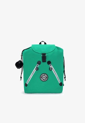 Grüner Stoff-Rucksack mit einer abgerundeten Klappe, ausgestattet mit silbernen Reißverschlüssen, einem Logo-Patch und einem flauschigen schwarzen Pompon-Schlüsselanhänger.