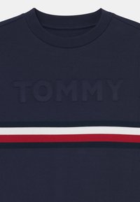 Navyblauwe sweatshirt met een ronde hals, met een verhoogd "TOMMY" logo en horizontale strepen in rood, wit en blauw over de borst.