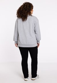 Grauer Sweatshirt mit lockerer Passform, langen Ärmeln, gerippten Bündchen und Saum, kombiniert mit schwarzen Hosen und silbernen Turnschuhen. Rückansicht angezeigt.