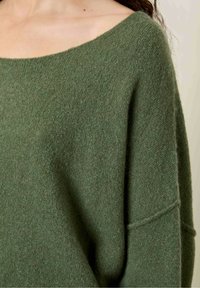 Oliven grønt sweater lavet af blødt, struktureret stof. Har en bred, off-shoulder halsudskæring og en løs, oversized pasform.