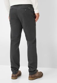 Pantaloni di cotone grigi con un design a gamba dritta, dotati di tasche posteriori con chiusura a bottone e orli rifiniti. Indossati con calzature marroni.