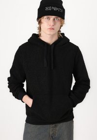 Czarna hoodie z teksturowanym materiałem z polaru, z kieszenią typu kangur, regulowanym kapturem i ściągaczami na rękawach. W komplecie z czarną czapką beanie.
