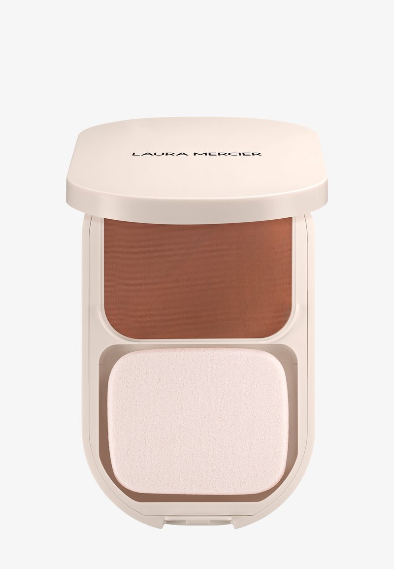Polvo compacto con un revestimiento de color beige claro, presenta un polvo marrón oscuro en la parte superior y un aplicador de esponja blanca en la parte inferior, con una textura suave.