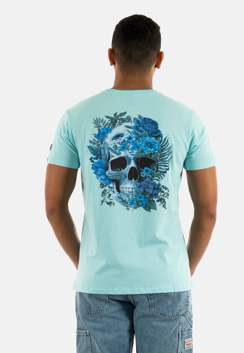 T-shirt en coton vert menthe avec un grand graphique de crâne floral bleu dans le dos, manches courtes et col rond classique.
