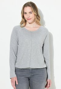 Grijze lange mouwen top van zachte stof, met een ronde halslijn, een ontspannen pasvorm en naaddetail in het midden. Gepaard met grijze jeans.